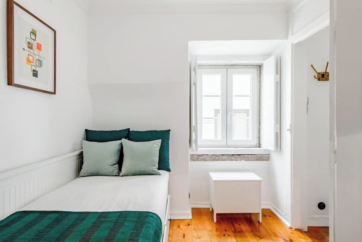 A bedroom with a bed, a window, a white radiator, and a small white table.