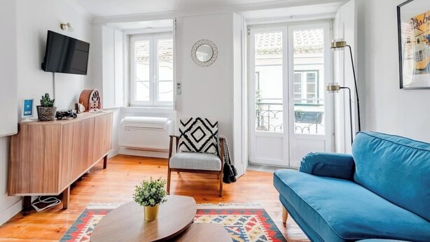 Ett vardagsrum med en blå soffa, ett träskåp, en tv och en fåtölj med ett geometriskt mönstrat kuddöverdrag.