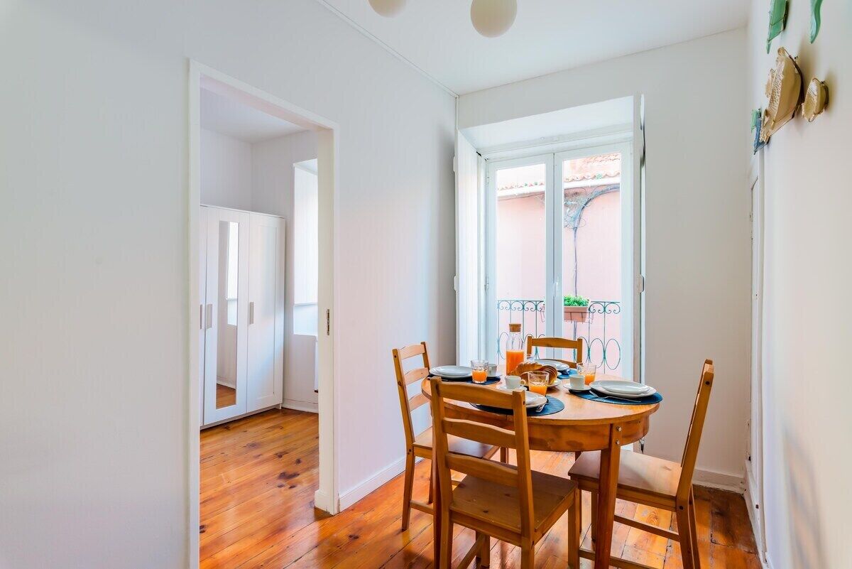 A dining area with a round table, chairs, and a window with a view of a balcony.