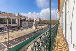 Ein Balkon mit Blick auf eine Stadtstraße, ein Denkmal und Gebäude mit Beschilderung.