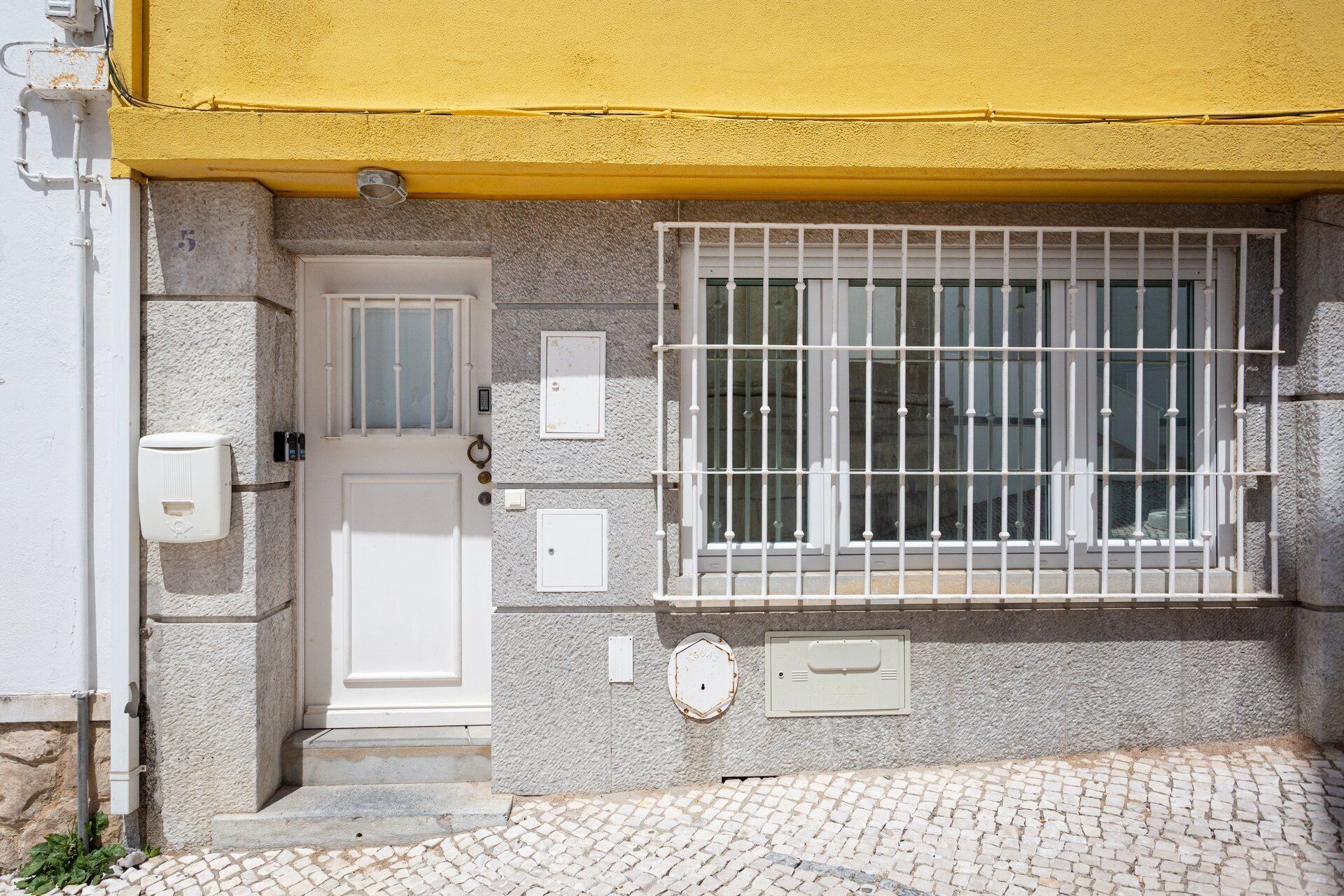 A building with a yellow awning, a barred window, a white door, and a stone wall.