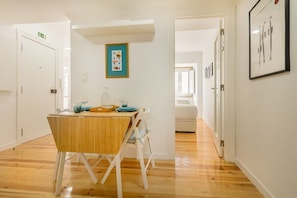 Ein Essbereich mit Holztisch und -stühlen, einem gerahmten Bild an der Wand und einem Flur, der in einen anderen Raum führt.