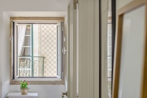 Ein Zimmer mit Fenster, einem Blumentopf und Blick auf einen Balkon mit Geländer.
