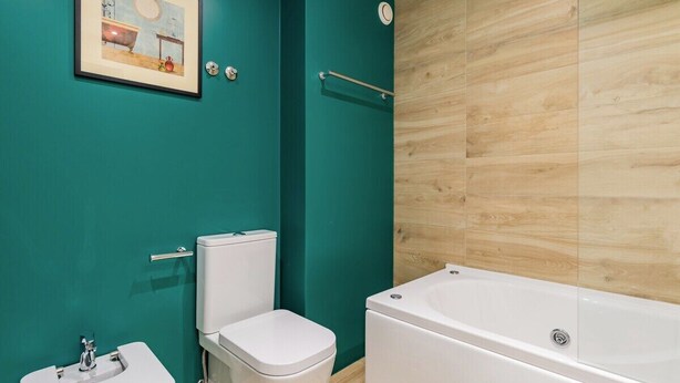 Een badkamer met turquoise wanden, een witte wastafel, een toilet en een bad.