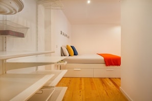Ein kleines Zimmer mit einem Bett, einem Schreibtisch und einem Wäschekorb.