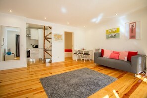 Ein modernes Wohnzimmer mit grauem Sofa, einer Holztreppe, einem Essbereich und einer Küche.