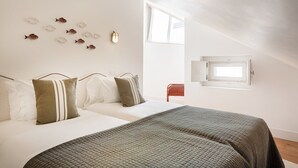 Une chambre à coucher avec un lit, des oreillers, une couverture matelassée, une lampe fixée au mur, une fenêtre et une chaise rouge.
