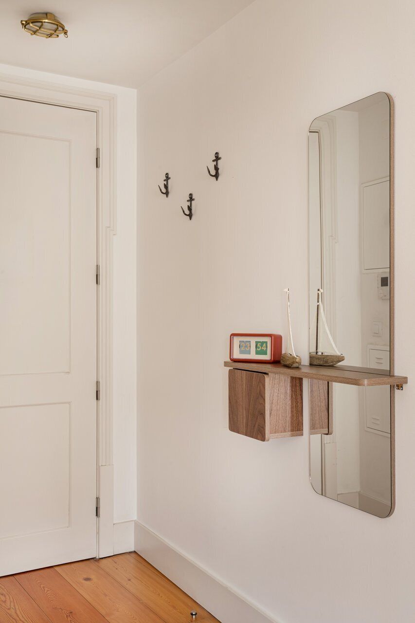 Een gang met een witte deur, een houten plank met een klok en een spiegel aan de muur.