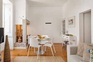 Ein modernes Wohnzimmer mit Essbereich, weißen Möbeln, einem Kamin und einer Küchenzeile.