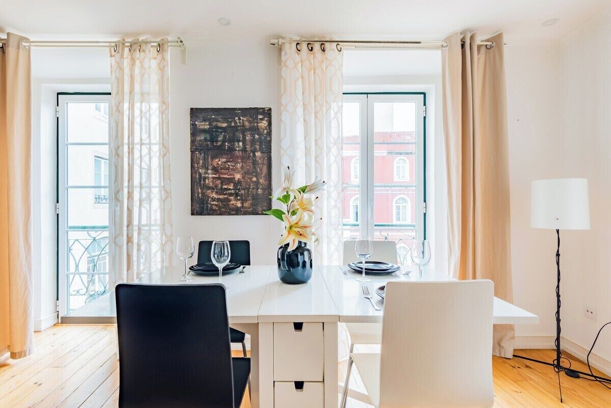 A dining area with a table set for two, a vase with flowers, and a painting on the wall.