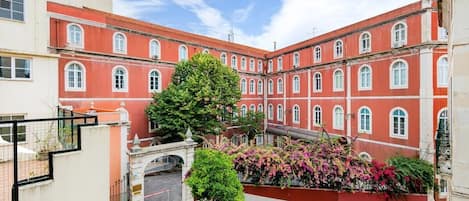 Un patio con un edificio rojo, un árbol y un cantero de flores.