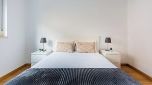 A bedroom with a bed, two bedside tables with lamps, a window, and a dark rug. - Olaias Park Flat (Lisbon)