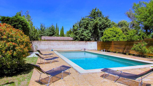 A rectangular swimming pool with a tiled deck, surrounded by a low brick wall and a wooden fence. - Amazing home in Lauris (Lauris)