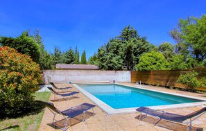 Une piscine rectangulaire, bordée d’une terrasse carrelée, entourée d’un petit muret en briques et d’une clôture en bois.