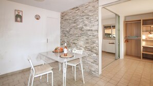 A dining area with a white table and chairs, a stone accent wall, and a kitchen visible through an open door. - Amazing home in Lauris (Lauris)