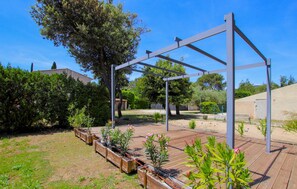 Ein Garten mit Holzterrasse, Metall-Pergola und verschiedenen Pflanzen.