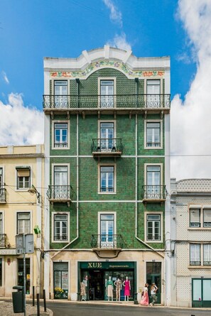 Ein mehrstöckiges Gebäude mit grüner Fassade, Balkonen und einem Ladenlokal mit der Aufschrift 'XUE Supermercado'.