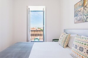 Hotellihuone, jossa on sänky, parvekeovi, josta avautuu näkymä kaupunkiin, ja seinälle asennettu pyöräteemainen taideteos.