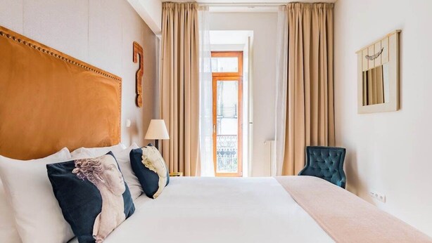 Habitación de hotel con una cama grande, cabecero, una silla, lámpara y vistas al exterior.