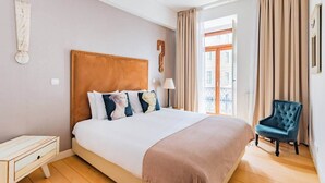 Habitación de hotel con una cama grande, una mesita de noche de madera, una silla y vistas al exterior.