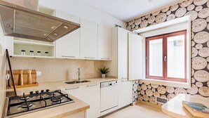 Una cocina con armarios blancos, una estufa a gas, un lavabo y una ventana con pared de madera.