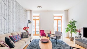 Una sala de estar moderna con un sofá, una mesa de centro, una silla roja, una silla gris, una mesita con una lámpara, una planta en maceta y un mueble para televisión.