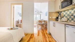 A compact kitchen with a microwave, a coffee maker, and a dishwasher. There is a dining area with a table and chairs, and a bed with a white comforter. - Bright Alfama Loft with Mezzanine | Guest Inn (Lisbon)