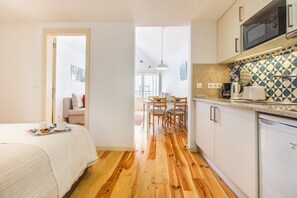 Eine kompakte Küche mit Mikrowelle, Kaffeemaschine und Geschirrspüler. Ein Essbereich mit Tisch und Stühlen sowie ein Bett mit weißer Tagesdecke.