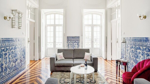 A room with a grey sofa, a small round table with a bottle and glass, and a red chair. - Downtown Chiado Treasure (Lisbon)
