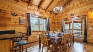 A wooden cabin interior with a dining table set for six, wooden chairs, a chandelier, and a sign listing cabin rules.