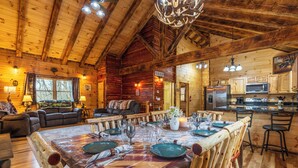 A log cabin interior with a dining area, kitchen, and living room.