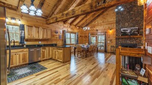 A wooden cabin interior with a kitchen, dining area, and stone fireplace.