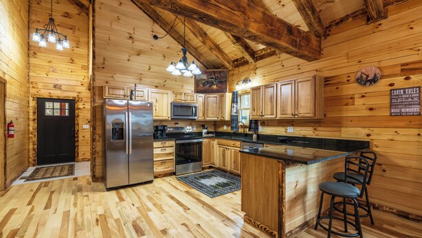 A wooden cabin interior with a kitchen area featuring a refrigerator, microwave, and wooden cabinets.