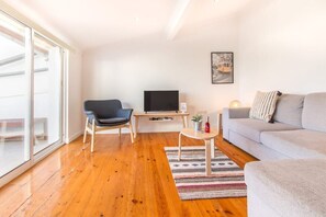 Ein modernes Wohnzimmer mit einer Couch, einem Sessel, einem Fernseher und einem kleinen Tisch mit einer Pflanze.