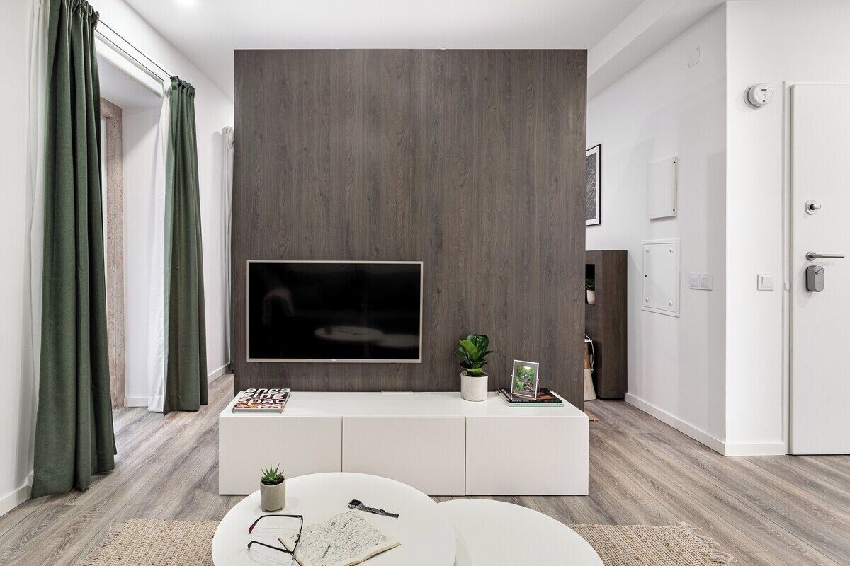 A modern living room with a flat-screen TV mounted on a white console, a small potted plant, and a magazine.