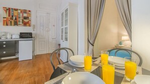 Un comedor con una mesa dispuesta para el desayuno, una cocina con electrodomésticos y una puerta que da a otra habitación.