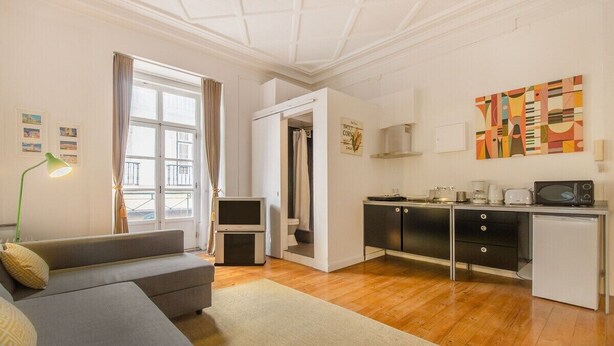Un espacio habitable compacto con sofá, kitchenette, televisor y ventana con cortinas.