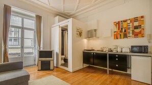 Un espacio habitable funcional con kitchenette, sofá, mesa de comedor y vistas amplias a través de un gran ventanal.