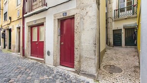 Eine enge Kopfsteinpflasterstraße mit Gebäuden, die rote Türen und Balkone haben.
