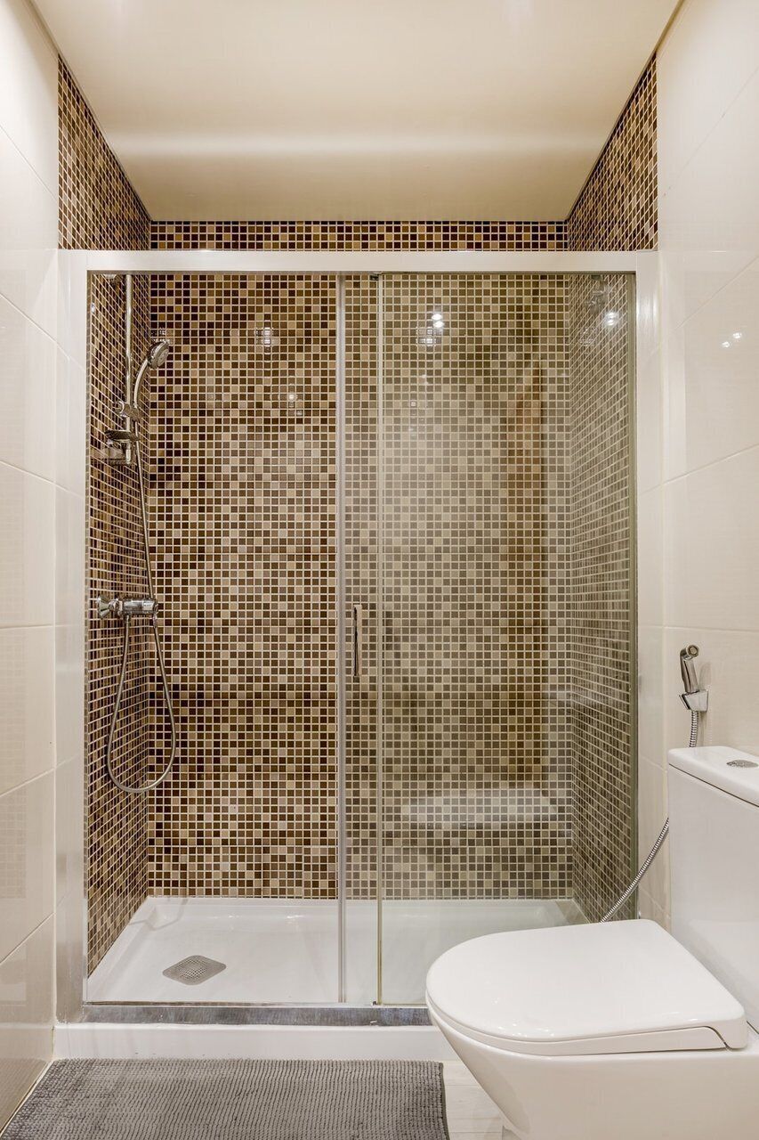 Een douche met mozaïektegels, een toilet en een douchekop.