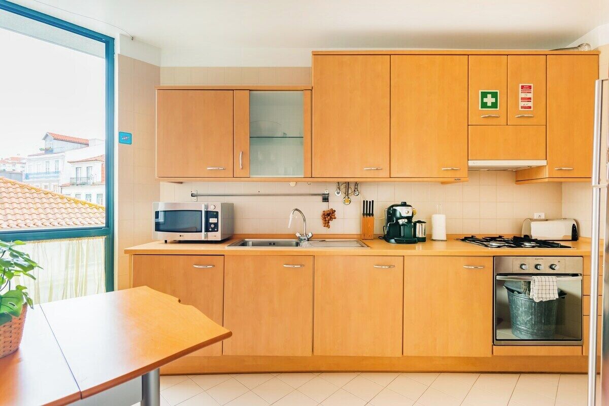 A modern kitchen with wooden cabinets, a microwave, a sink, a stove, and a window with a view of buildings.