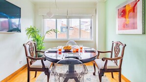 Un comedor con una mesa redonda, sillas, una planta en maceta y un ventanal con vistas a edificios.