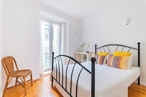 Ein Schlafzimmer mit einem Bett, einem Sessel, einem Fenster und einer weißen Wand.