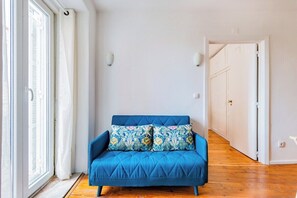Ein Zimmer mit einem blauen Sofa, einem gemusterten Kissen, einer weißen Wand und einem Holzboden.