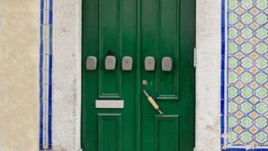 Una puerta verde doble con el número '55' encima, una pared de azulejos con un diseño geométrico y una calle empedrada.