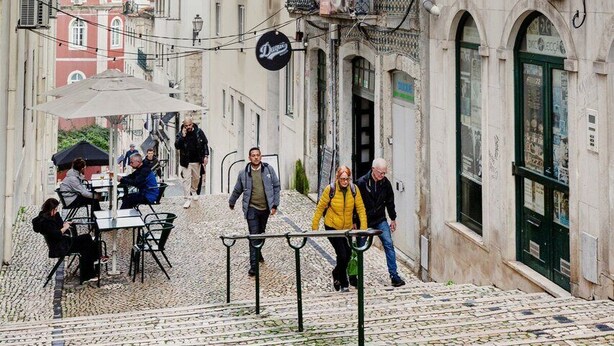 Una calle estrecha con adoquines, edificios con balcones y mesas al aire libre para cafés.