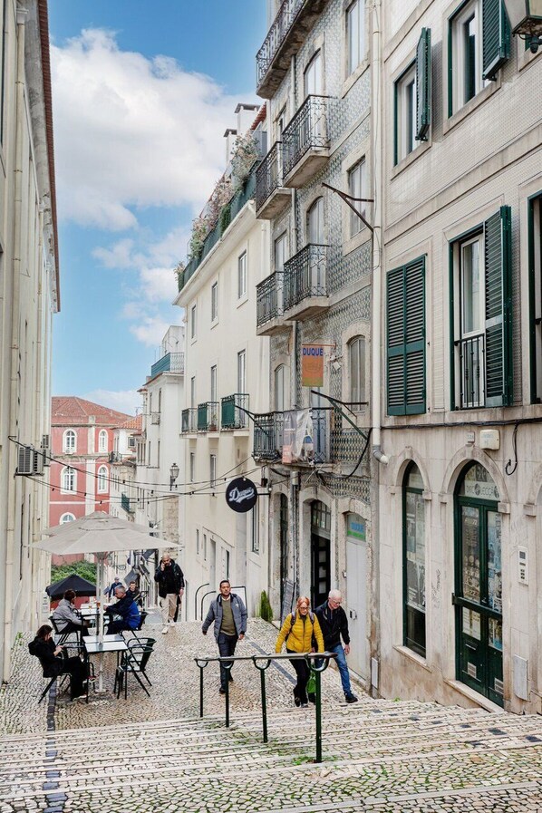Eine schmale Straße mit Kopfsteinpflaster, Häuser mit Balkonen und Außenbestuhlung für Cafés.
