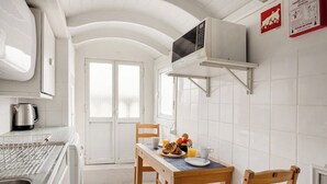 Una cocina con azulejos blancos, microondas, tetera y una mesa dispuesta para el desayuno.