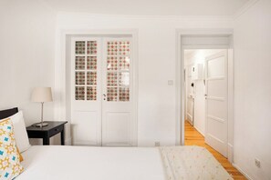 Ein Schlafzimmer mit Bett, Nachttisch, Lampe, einer verzerrten Tür und einem Flur, der in einen anderen Raum führt.