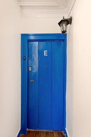 Eine blaue Tür mit dem Buchstaben 'E', eine Wandleuchte und ein Holzboden.